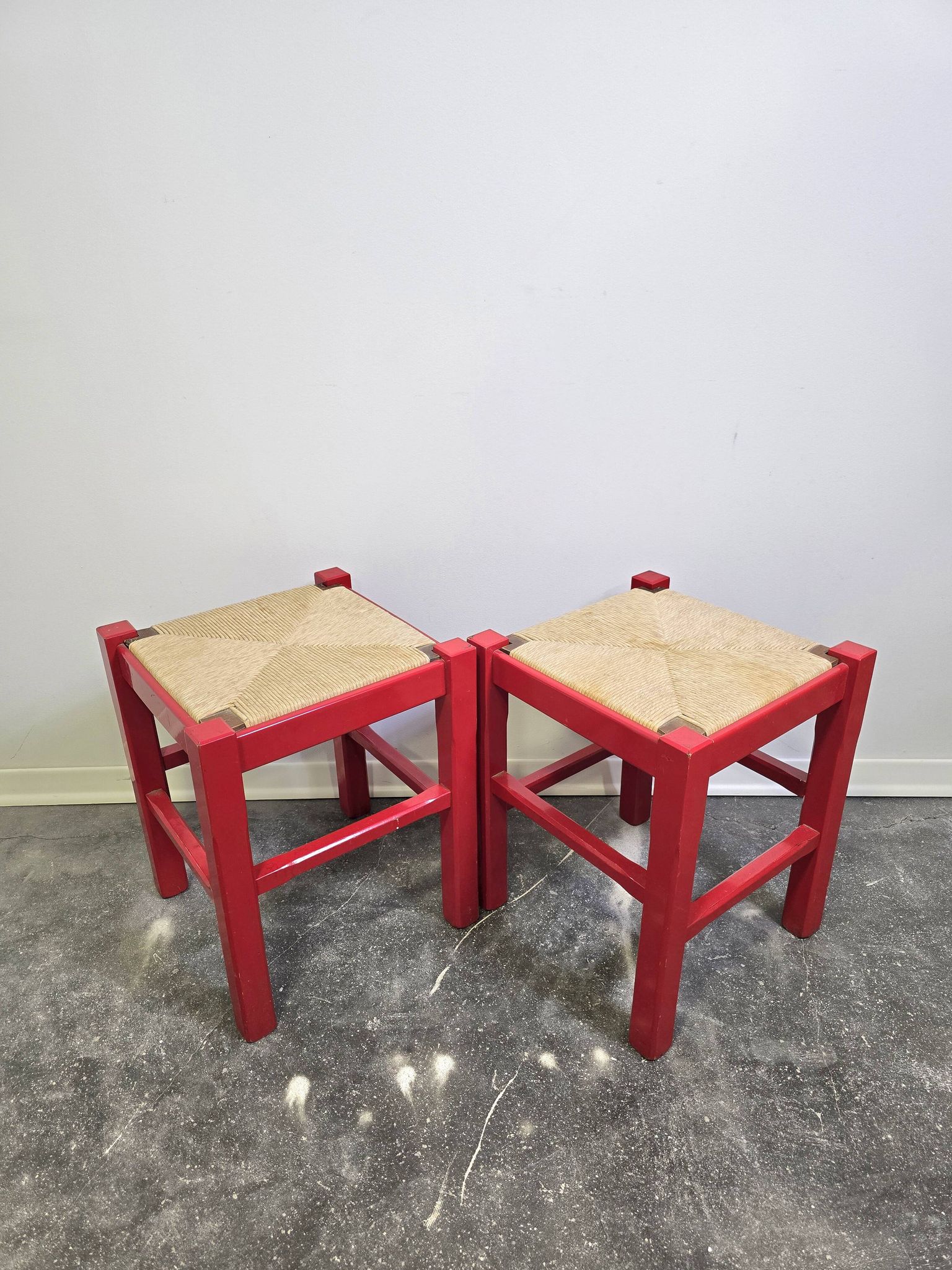 Red wooden stool with a woven straw seat.