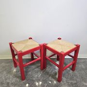 Red wooden stool with a woven straw seat.