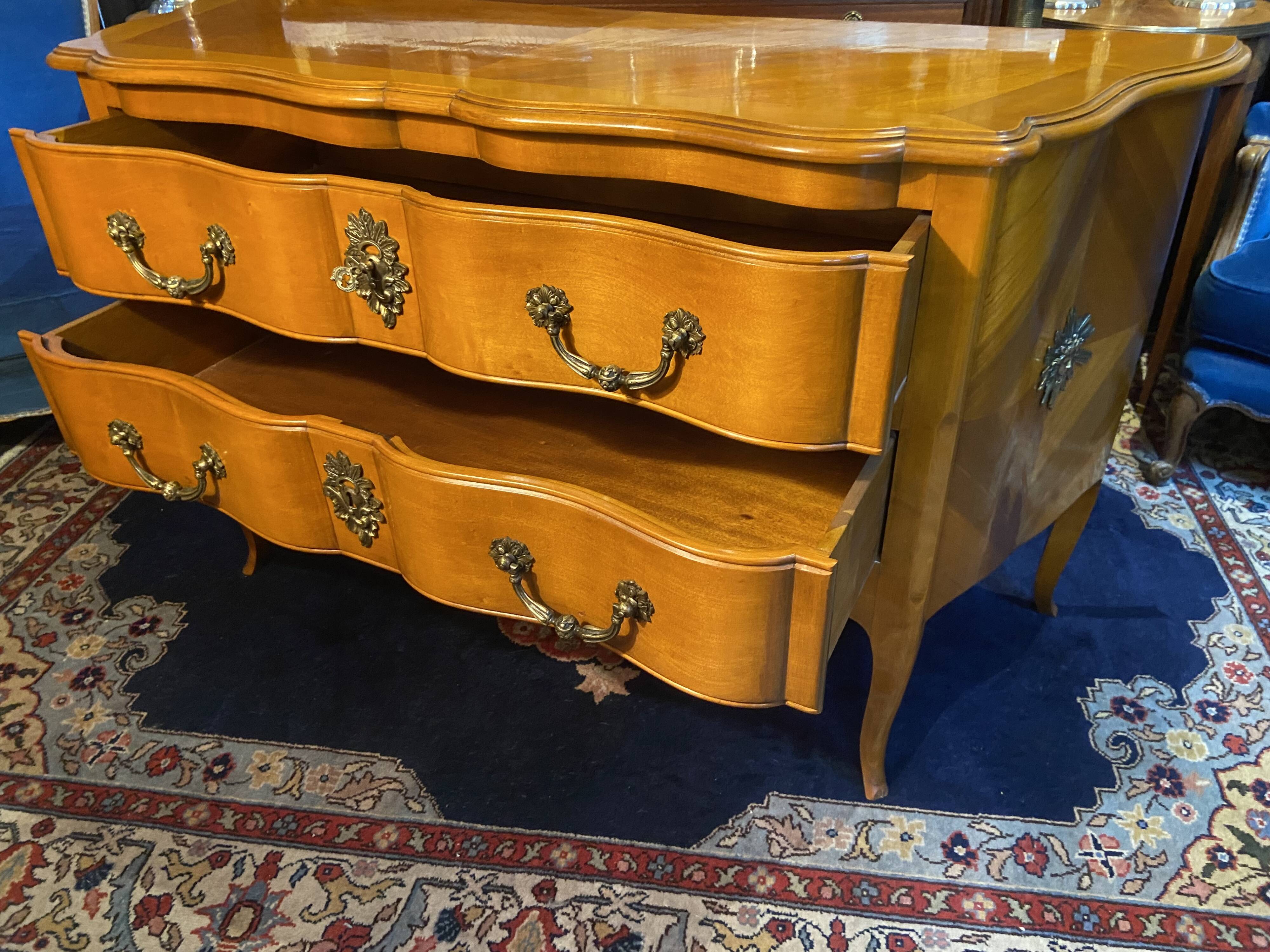 Large bow-fronted chest of drawers in blonde cherry with bronze ornamentation.