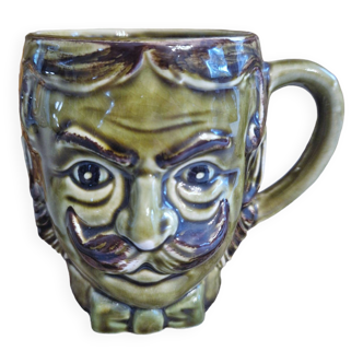 A collectible mustache tankard or cup in vintage ceramic, head of a man with a green mustache or