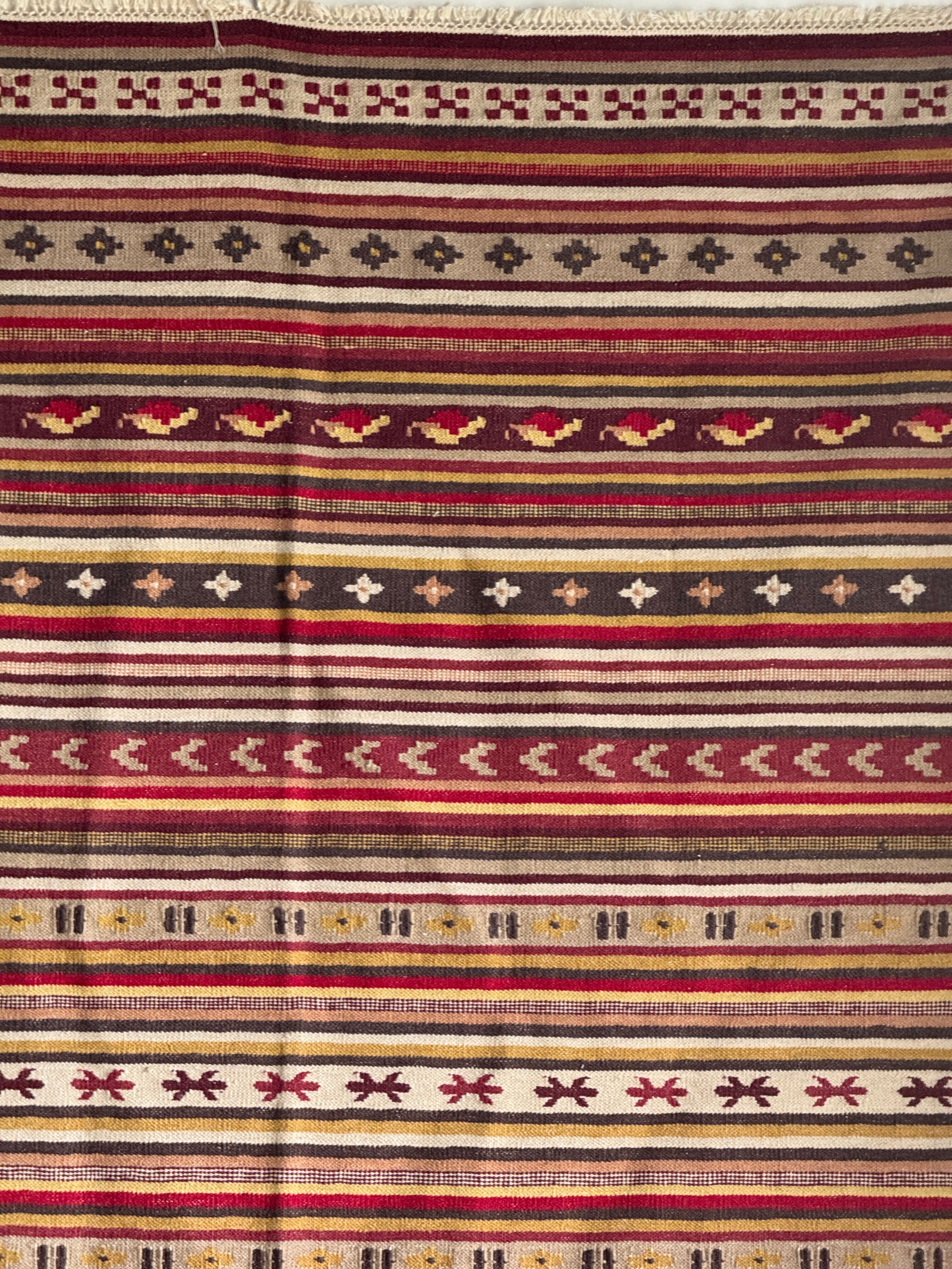 Large Indian rug with red, yellow, and white stripes and geometric fringes.