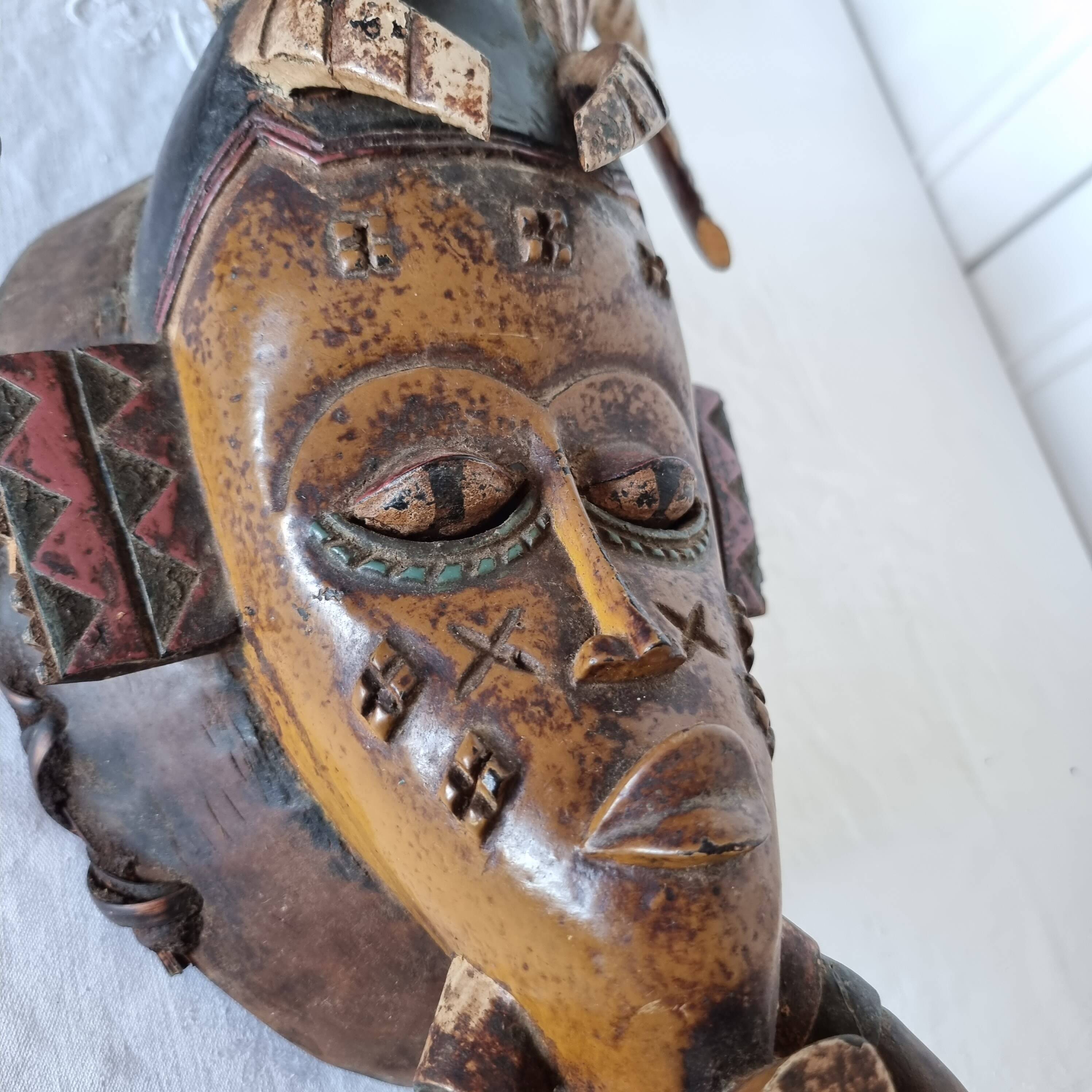 A large Senufo mask made of colored wood, decorated with an anthropomorphic figure