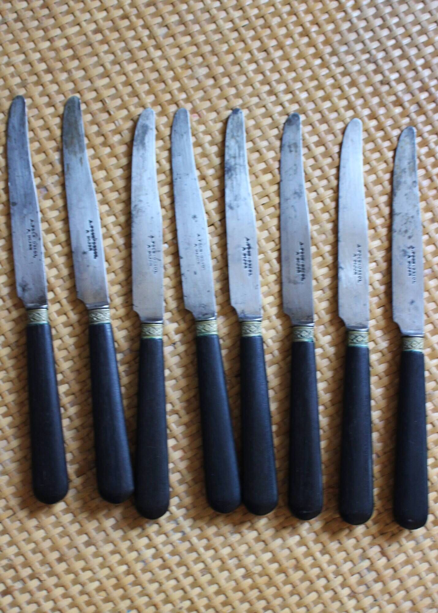 A set of 8 knives with black wooden handles and bolsters.