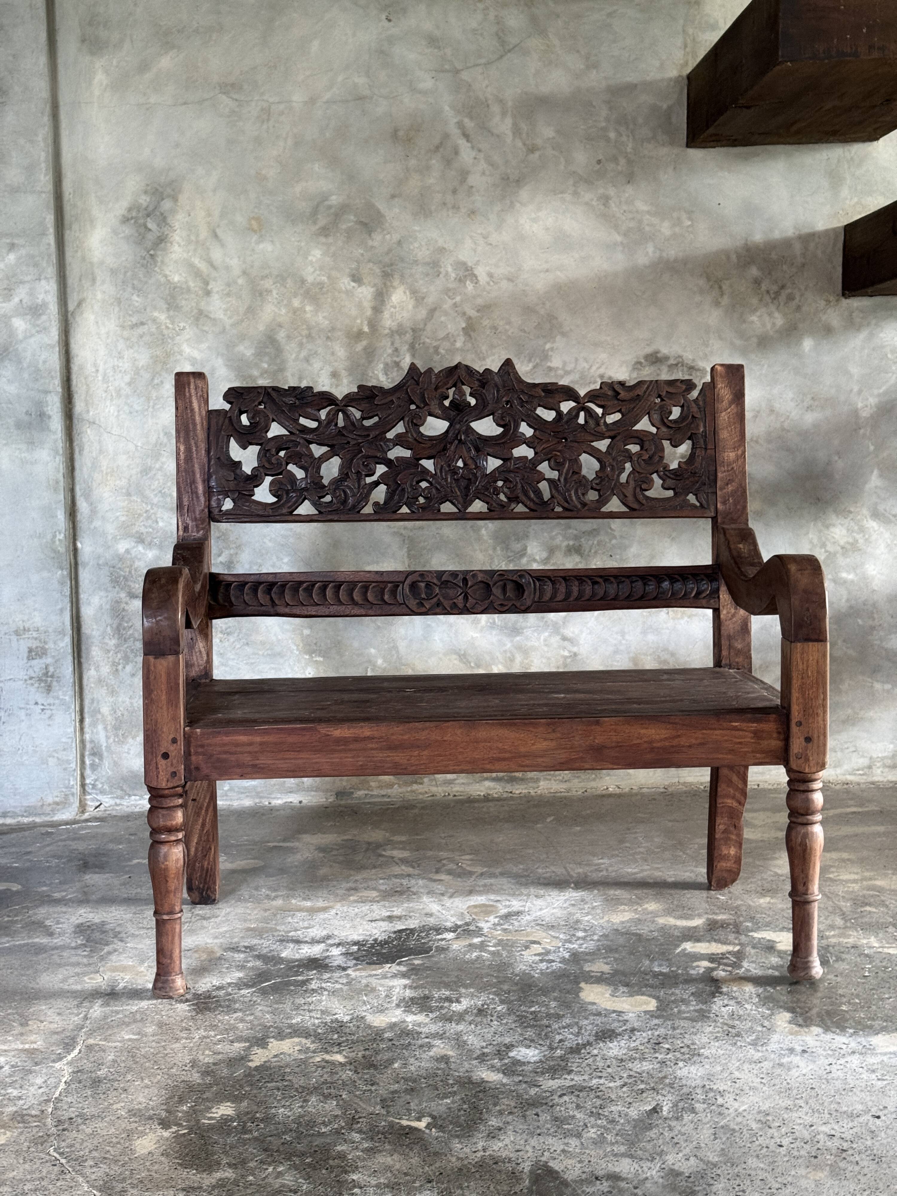Small antique Indonesian bench in carved teak with plant and floral motifs.