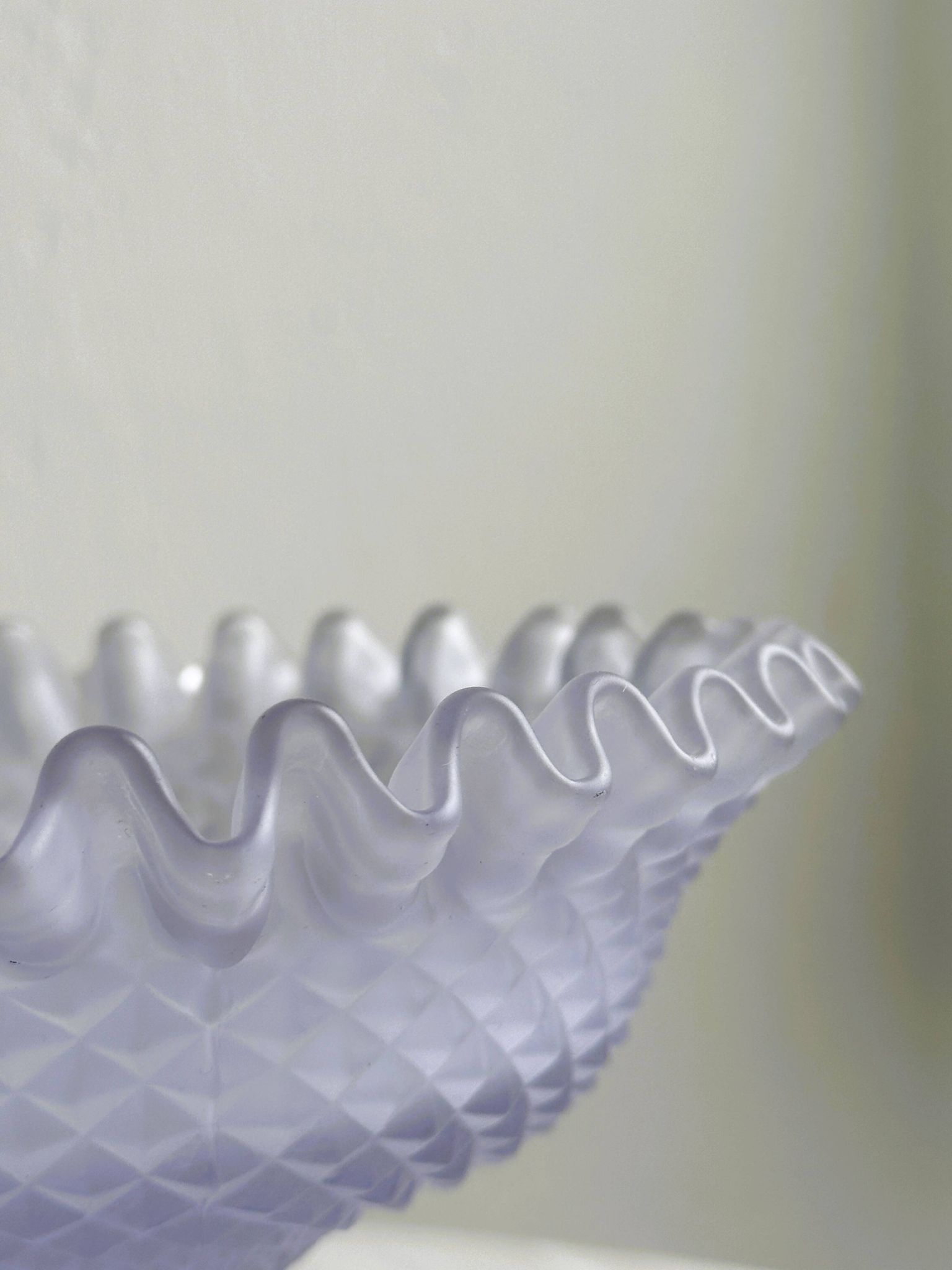 Purple glass pedestal bowl with wavy border and relief pattern.
