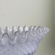 Purple glass pedestal bowl with wavy border and relief pattern.