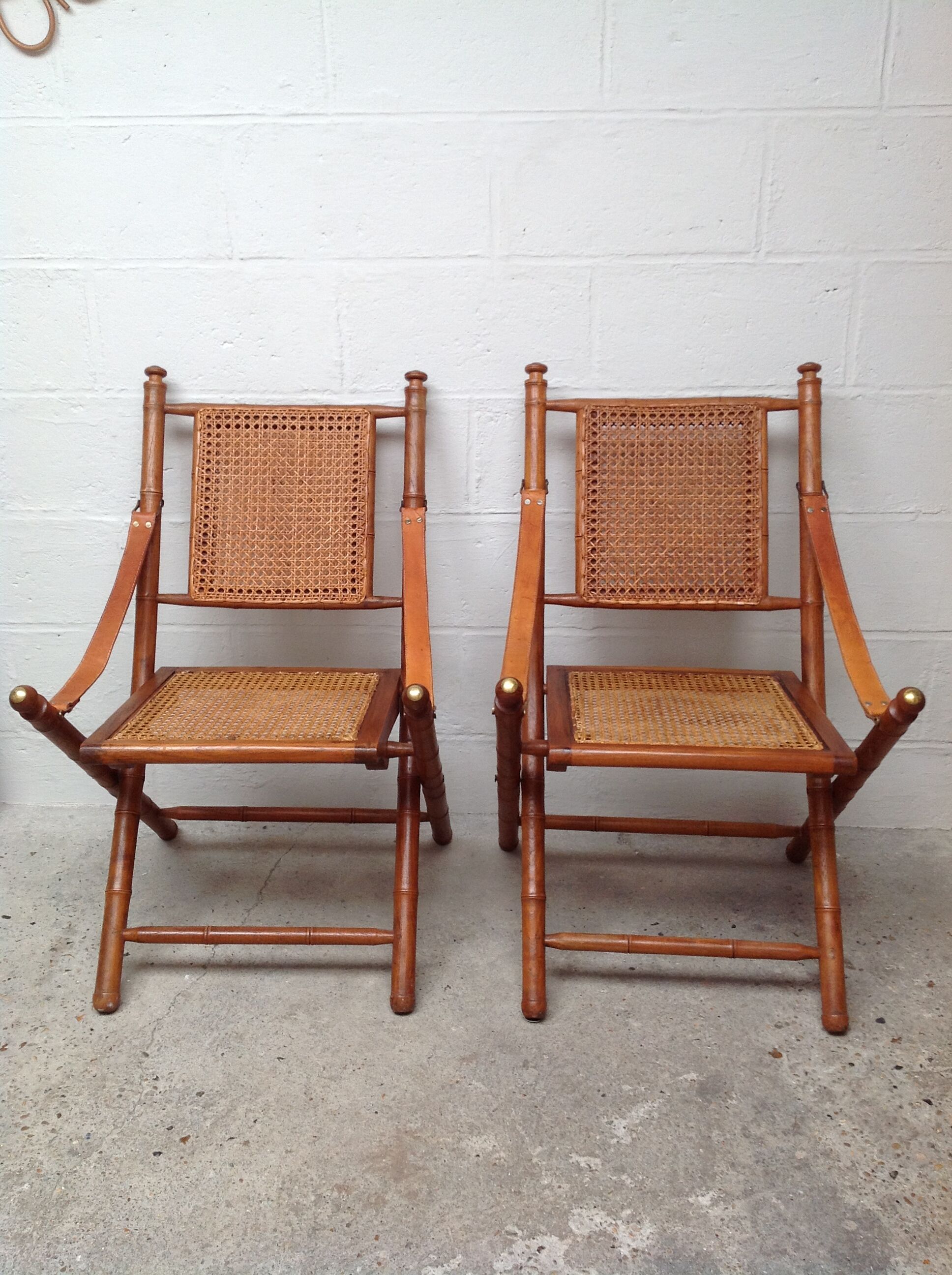 Pair of folding chairs in bamboo and caning, leather and brass