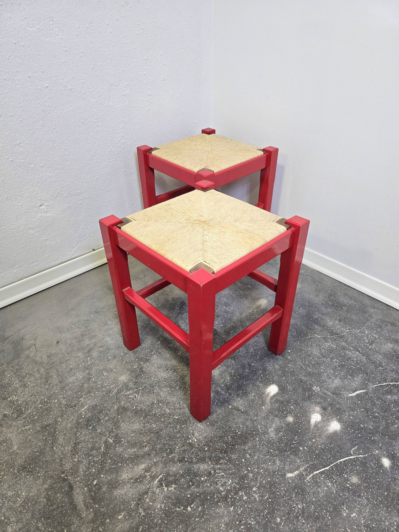 Red wooden stool with a woven straw seat.