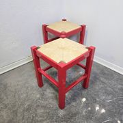 Red wooden stool with a woven straw seat.