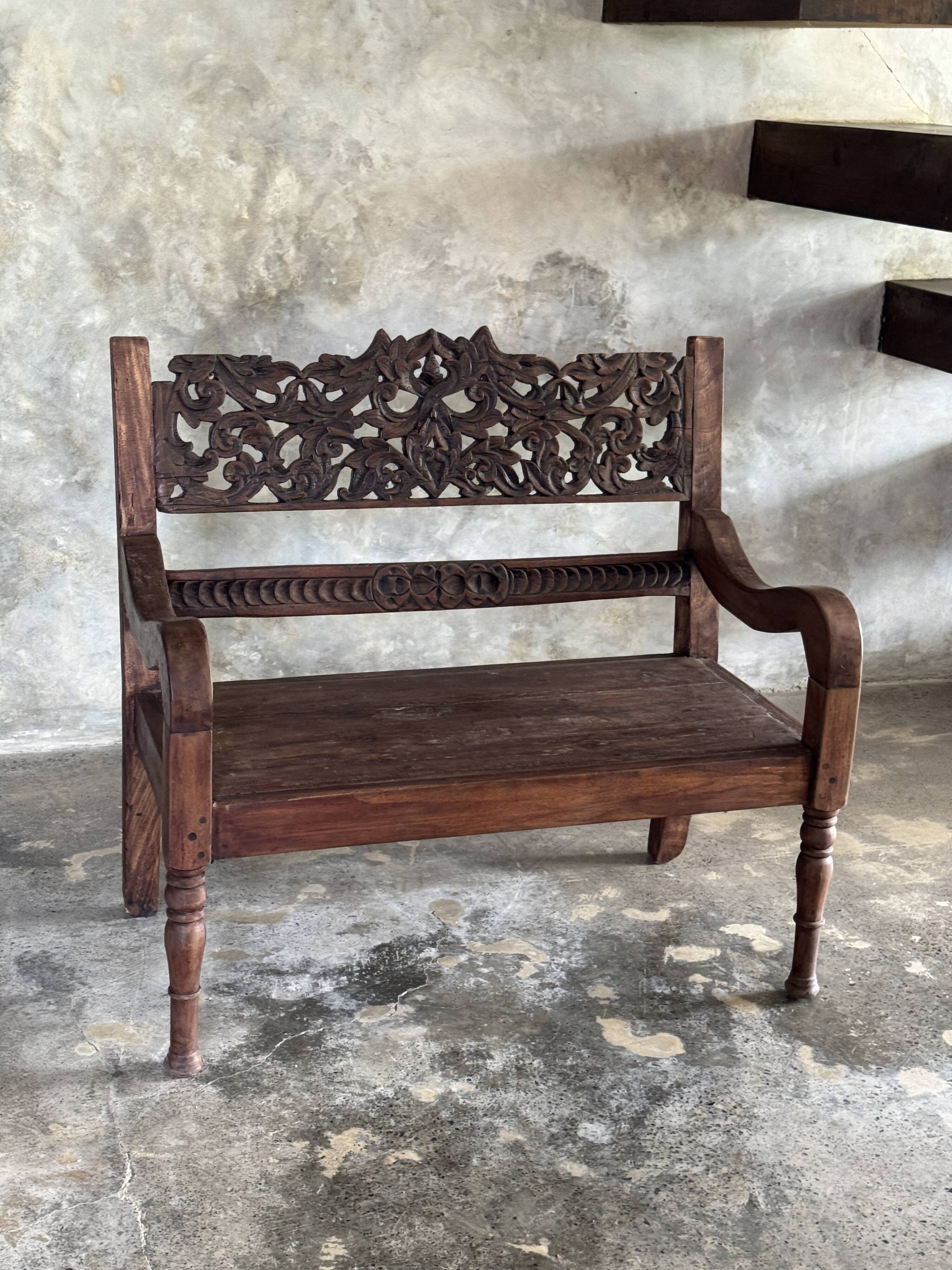 Small antique Indonesian bench in carved teak with plant and floral motifs.