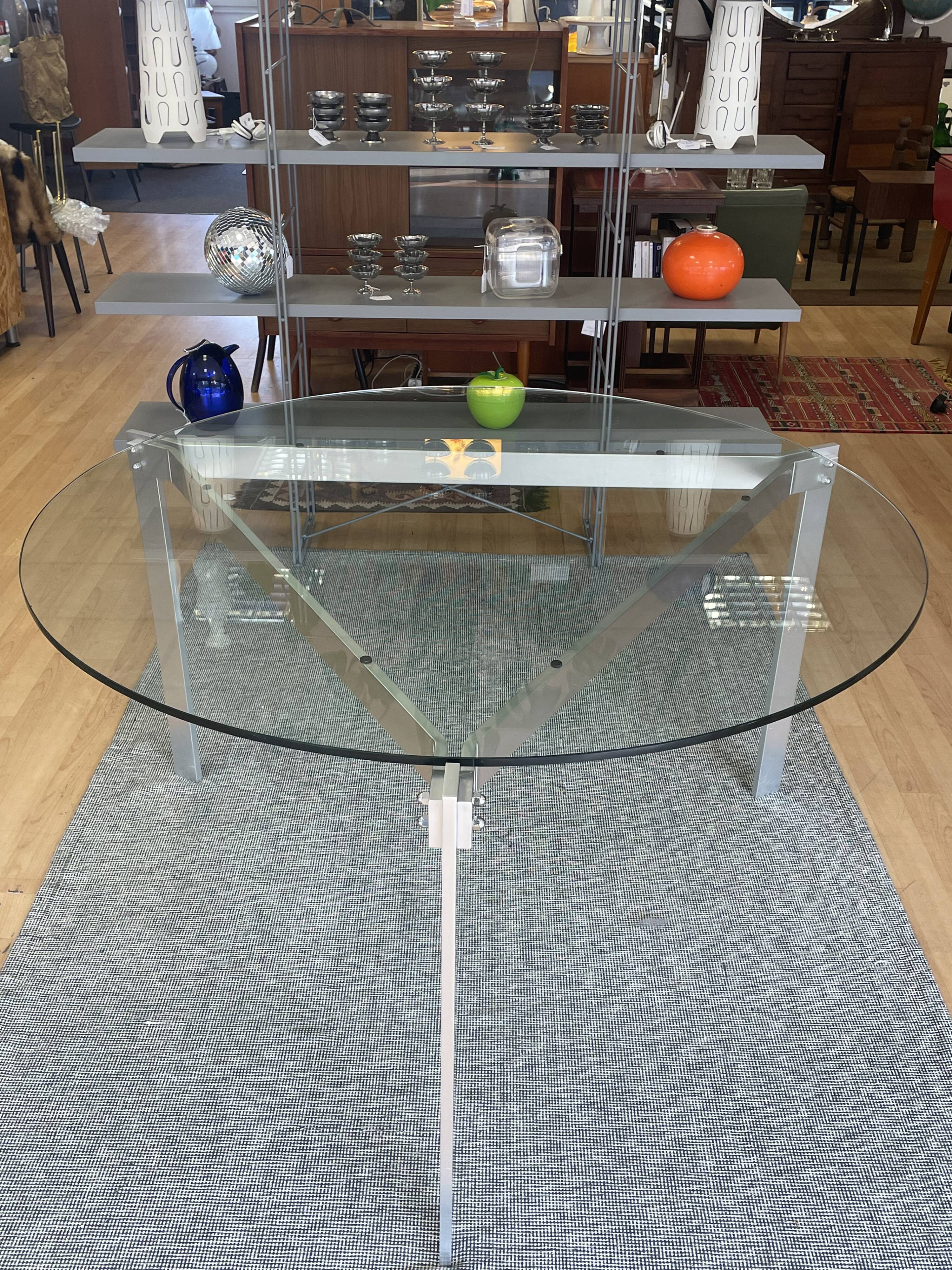 Round dining table with a glass top and brushed metal triangular frame.