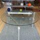 Round dining table with a glass top and brushed metal triangular frame.