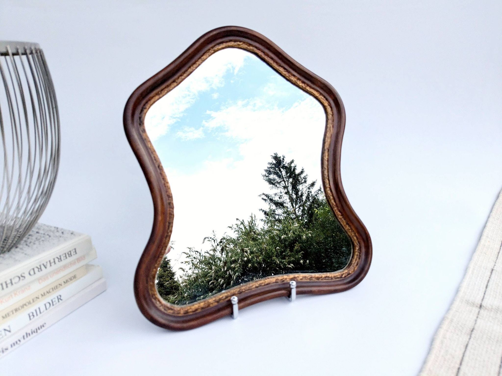 Antique wall mirror in carved wood with a wavy shape and a golden trim.