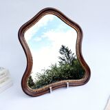 Antique wall mirror in carved wood with a wavy shape and a golden trim.