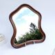 Antique wall mirror in carved wood with a wavy shape and a golden trim.