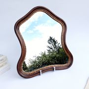 Antique wall mirror in carved wood with a wavy shape and a golden trim.