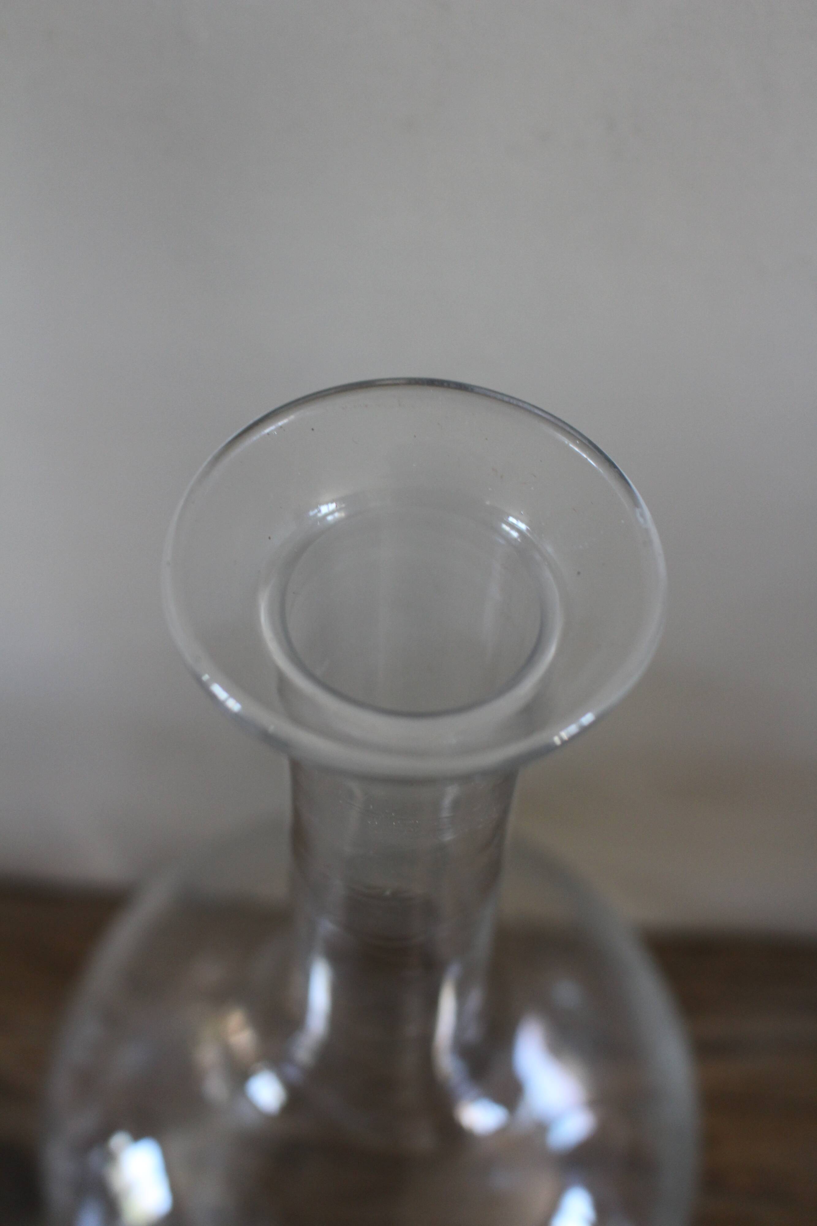 Antique glass carafe with a round belly and floral neck.