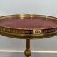 Guéridon rond de style néoclassique en laiton à piètement décoré de dauphins et plateau de celluloïde rouge cerclé d'une gallerie ajourée attribué à la Maison Jansen