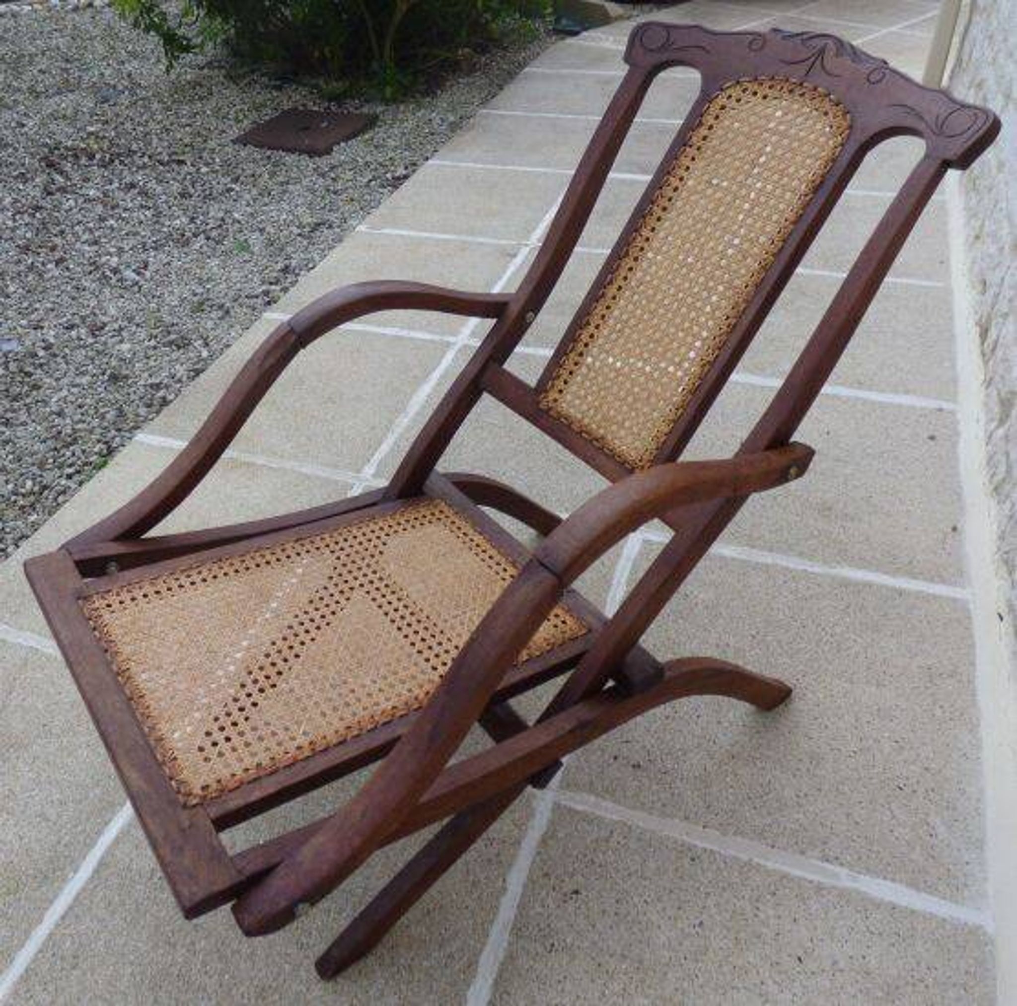 Antique folding chair with caned seat and backrest made of wood.