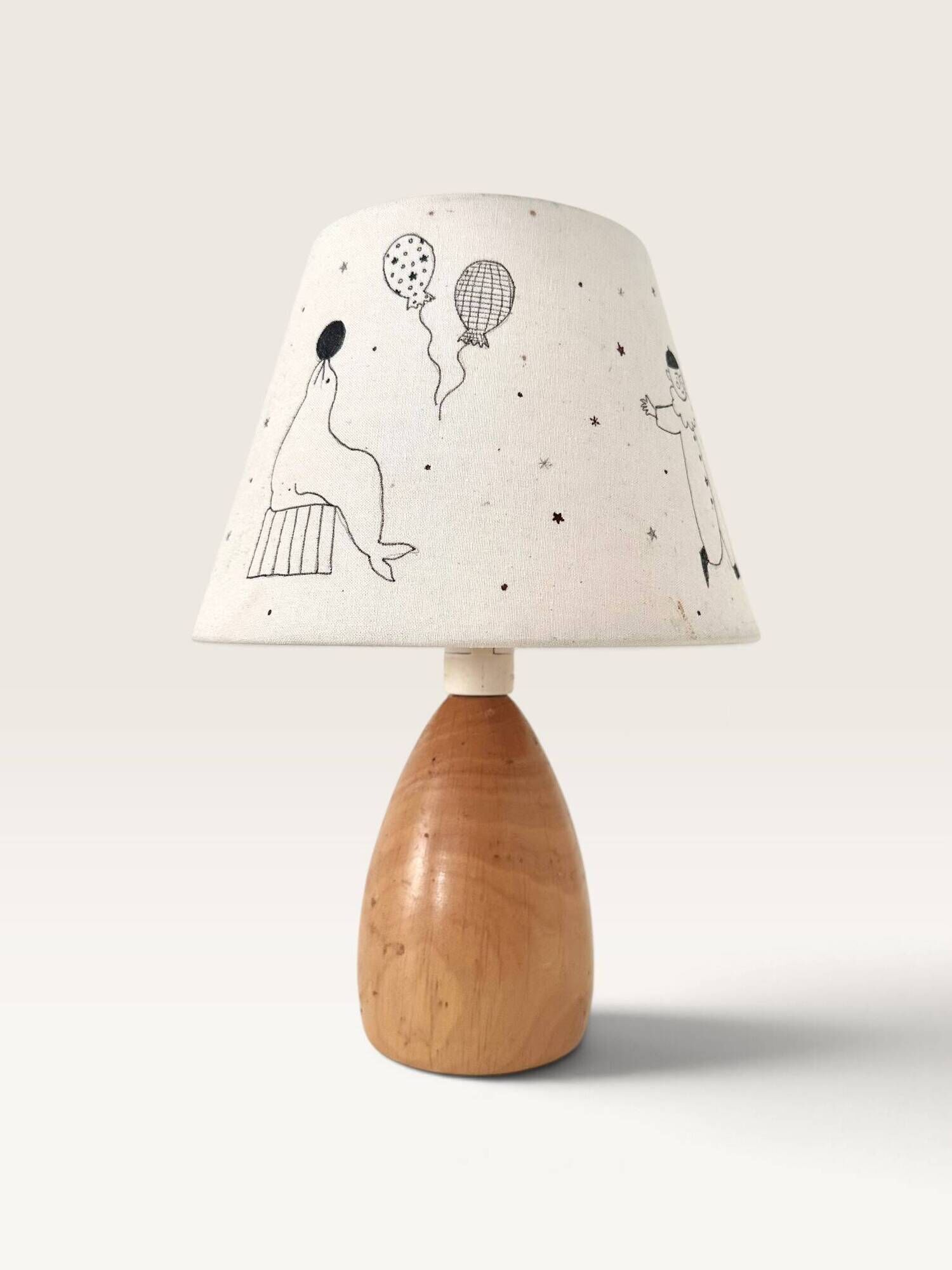 Wood-turned lamp with a hand-drawn lampshade, circus patterns.