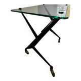 Vintage table with thick glass top and black steel legs with casters.