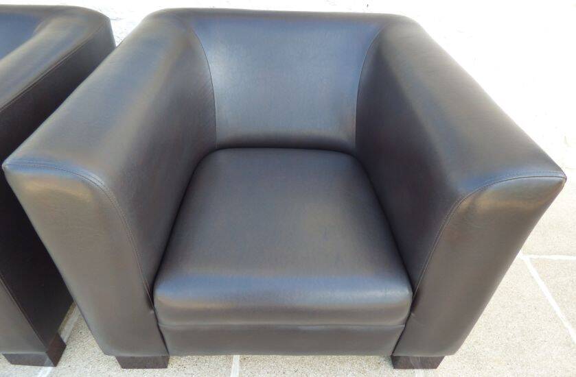 2 club armchairs with a chocolate faux leather seat and backrest and wooden legs.