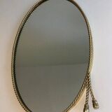 Oval brass mirror surrounded by a cord.
