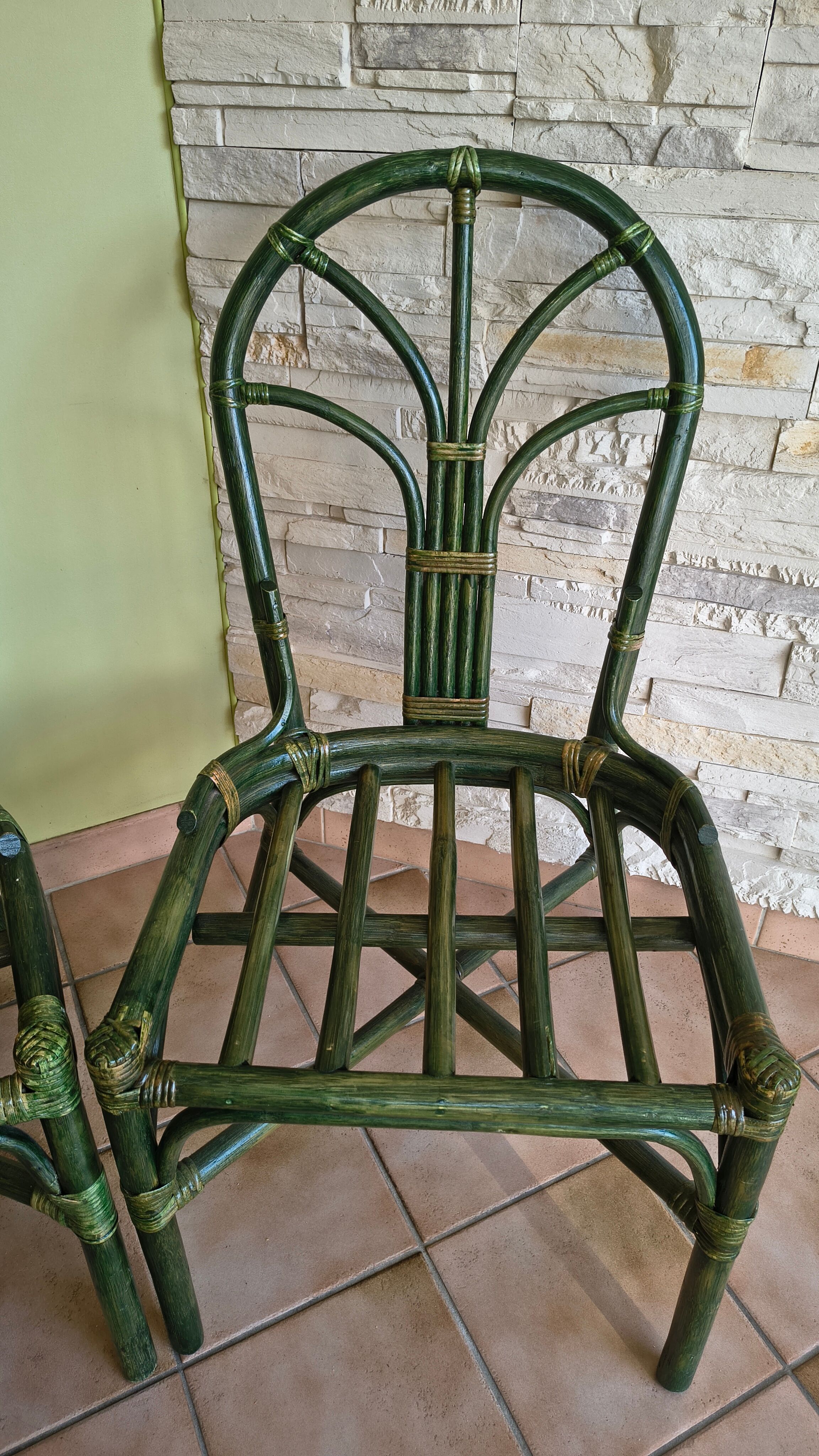Round rattan table with glass top and 4 green rattan chairs.