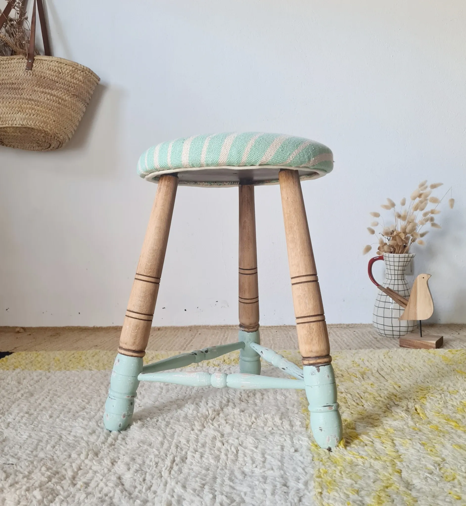 Antique tripod stool with blue striped seat.