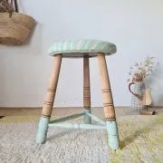 Antique tripod stool with blue striped seat.