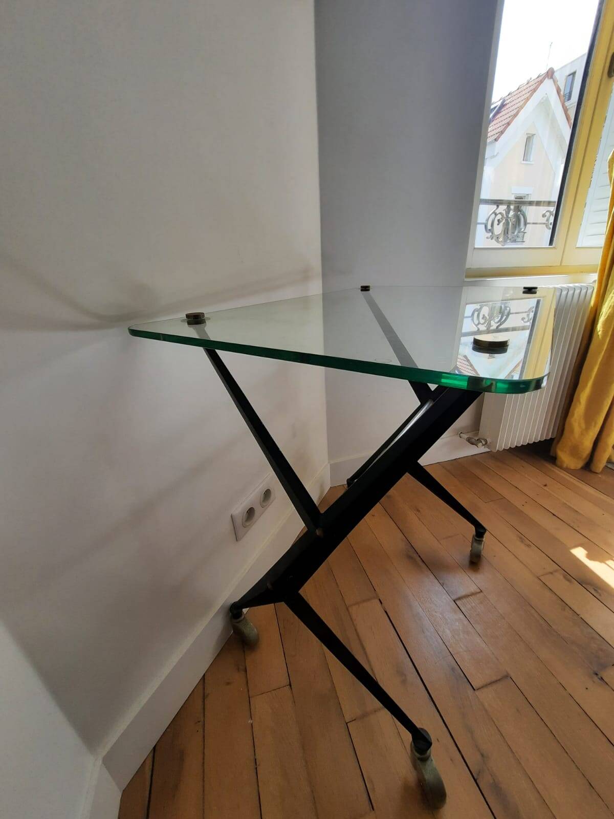 Vintage table with thick glass top and black steel legs with casters.