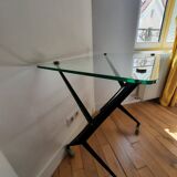 Vintage table with thick glass top and black steel legs with casters.