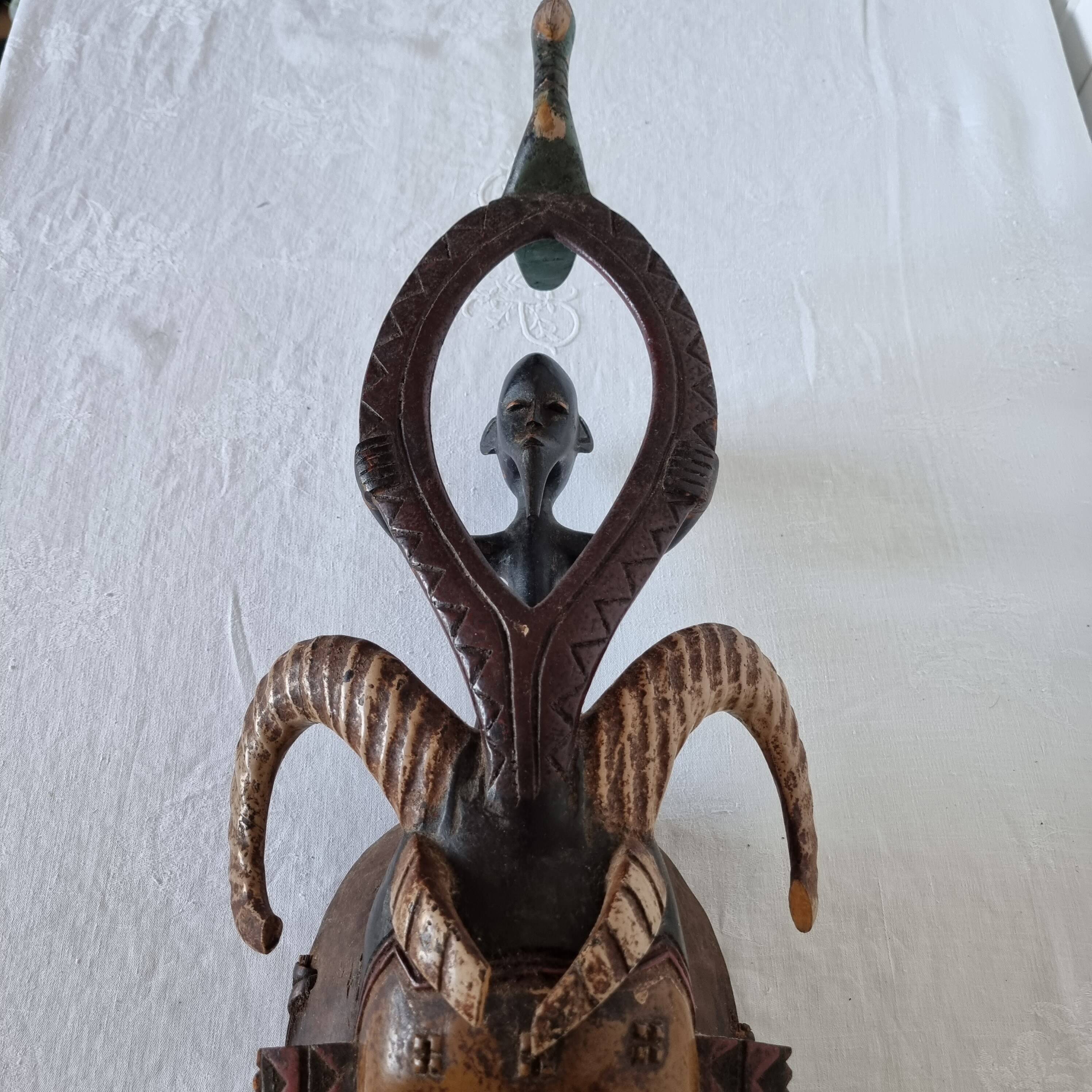 A large Senufo mask made of colored wood, decorated with an anthropomorphic figure