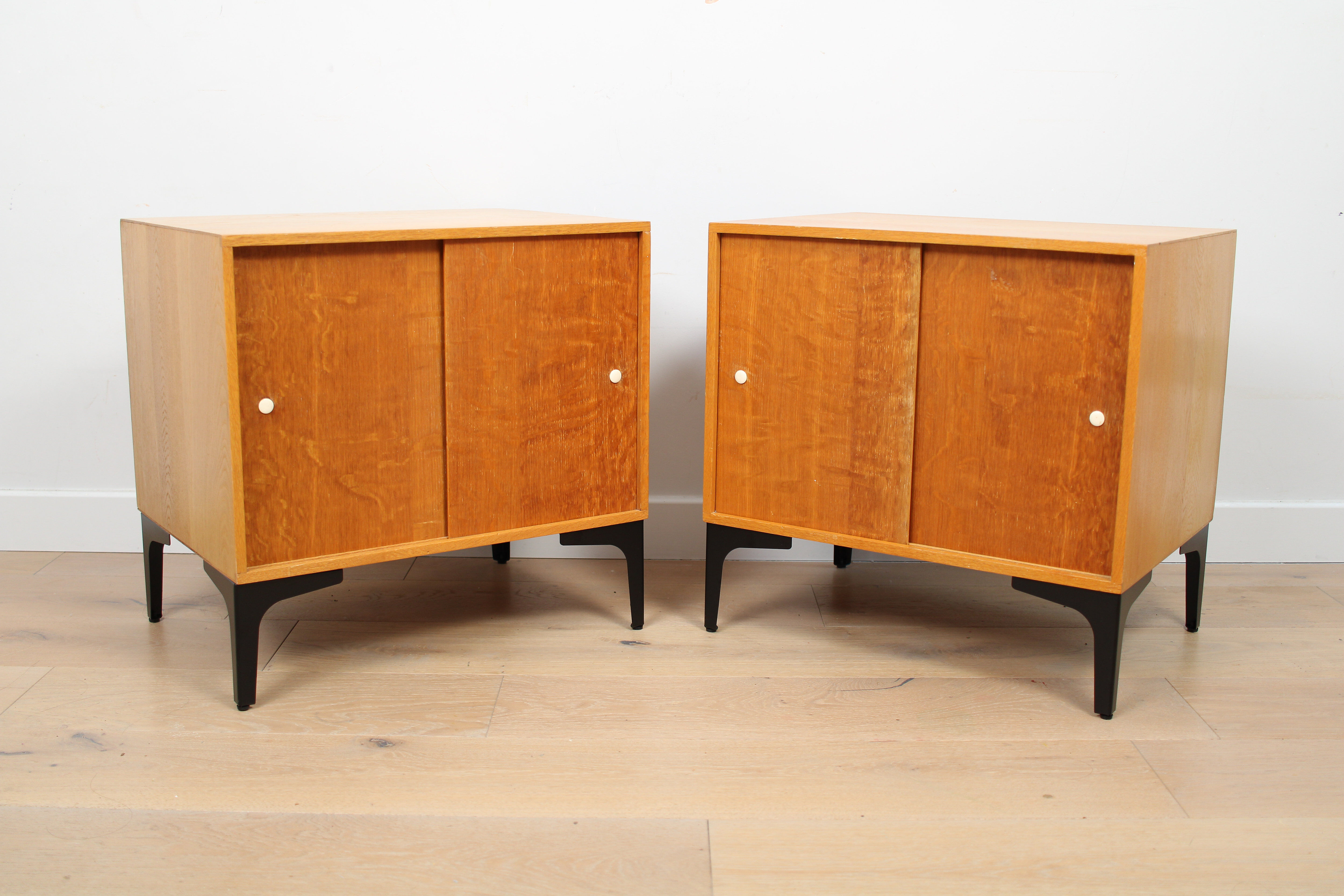 A pair of vintage mid-century bedside tables with oak sliding doors