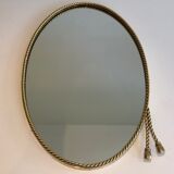 Oval brass mirror surrounded by a cord and adorned