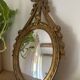 Oval convex witch mirror with golden ribbon mouldings.