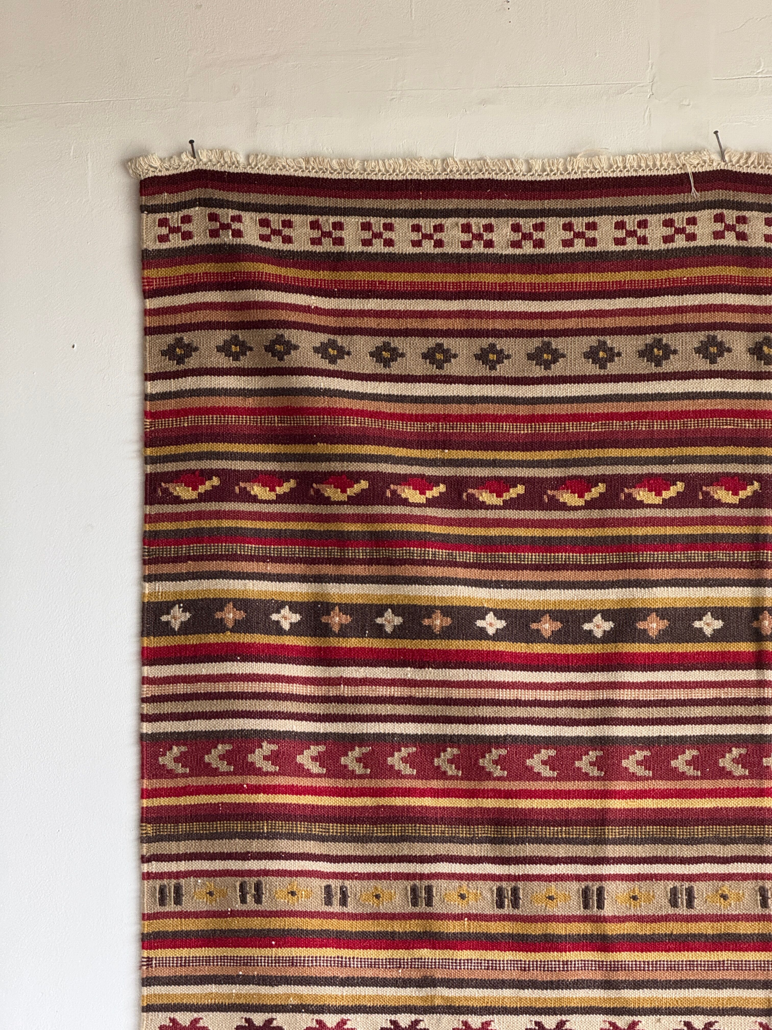 Large Indian rug with red, yellow, and white stripes and geometric fringes.