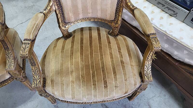 A pair of gilded wooden armchairs in the Louis XVI style.