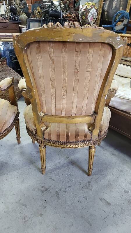 A pair of gilded wooden armchairs in the Louis XVI style.