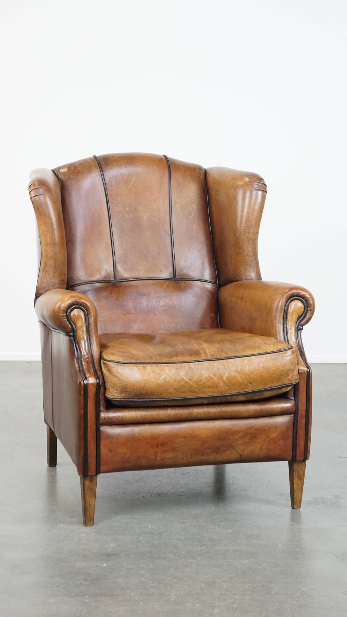Cognac-colored sheep leather wingback chair finished with black piping