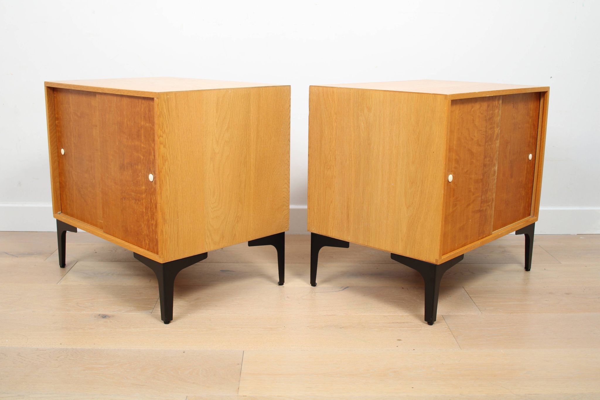 A pair of vintage mid-century bedside tables with oak sliding doors