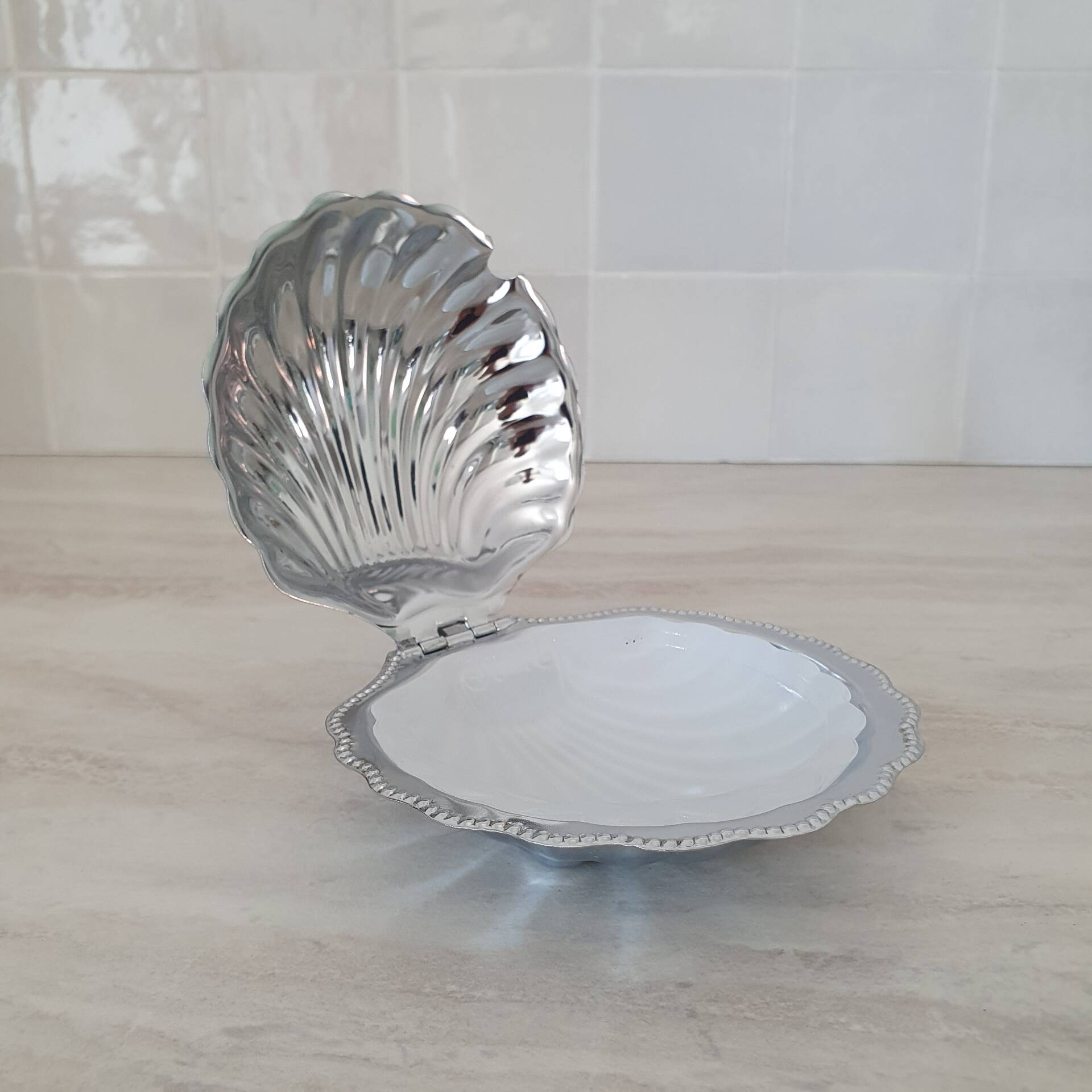 Scallop shell butter dish in stainless steel with its white glass saucer.
