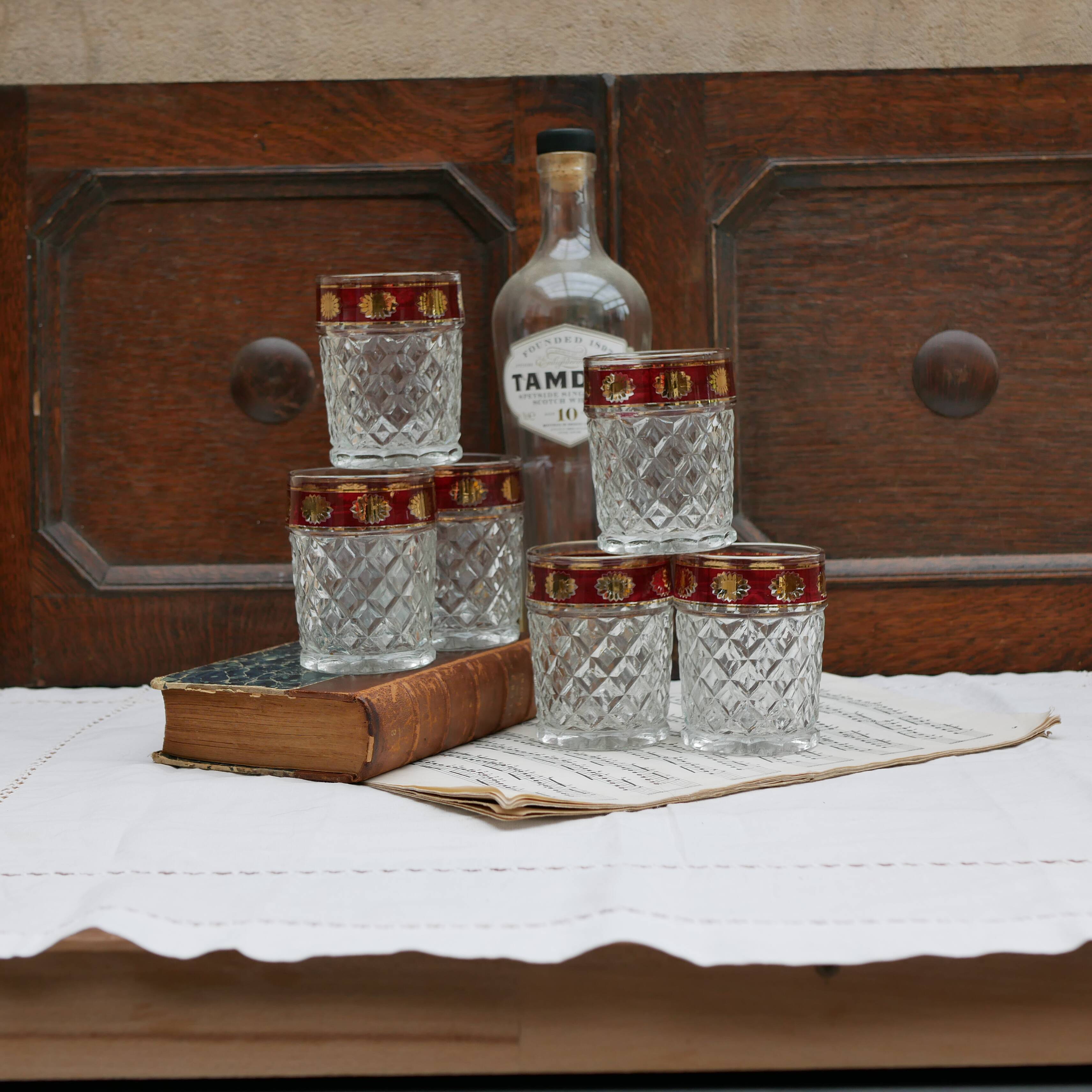 Six pressed glass whisky glasses with red and gold rims