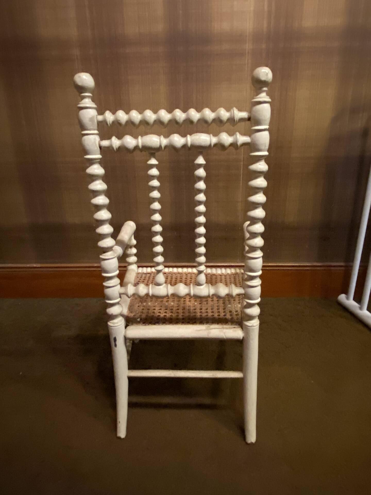 Antique wooden child's chair with turned legs and caning, white patina.