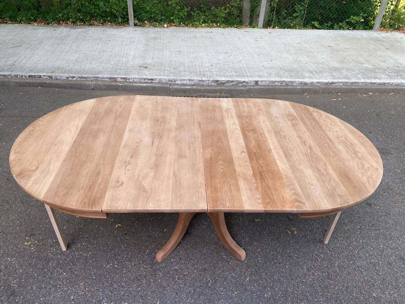 Large extendable round dining table stripped in solid cherry wood with a central leg.