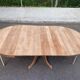 Large extendable round dining table stripped in solid cherry wood with a central leg.