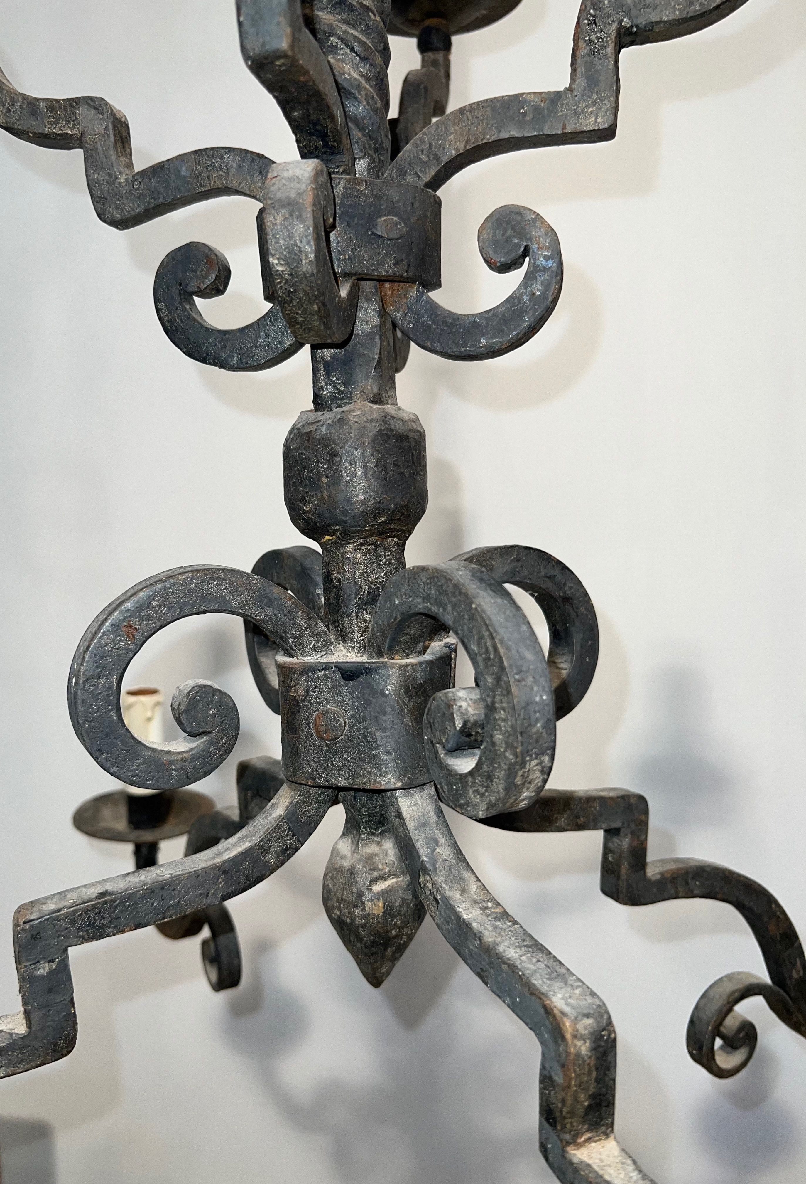 Two-tiered wrought iron chandelier with eight light arms in Gothic style.