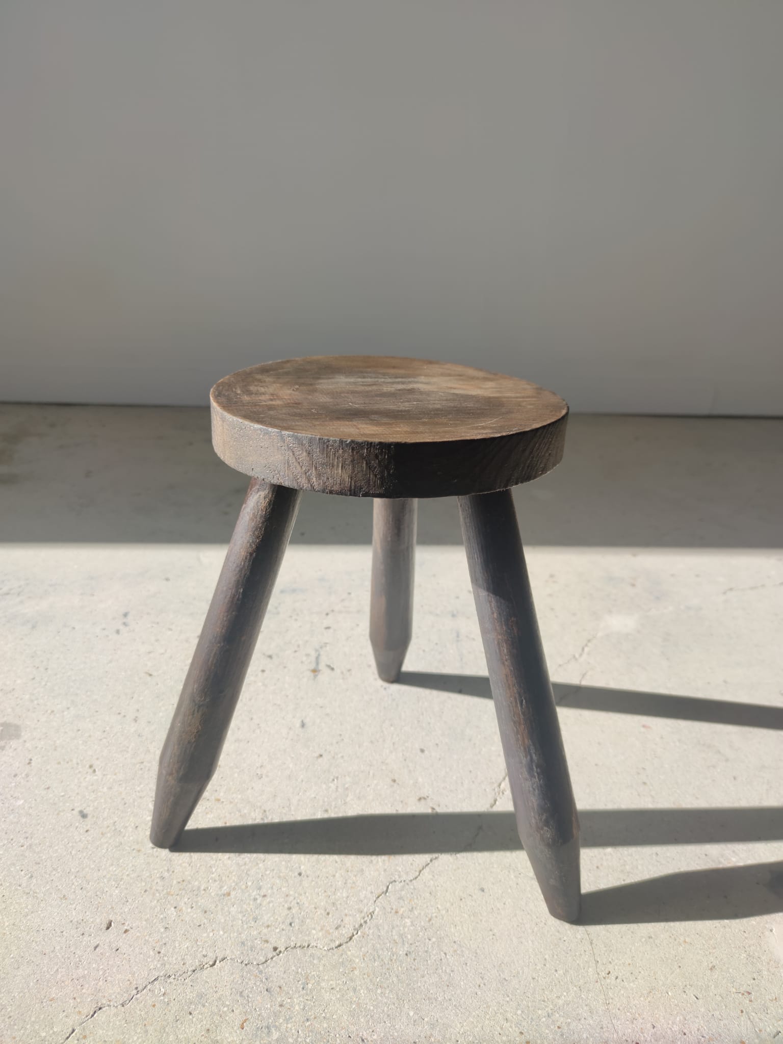 Small brutalistic tripod stool in dark wood tapered feet circular seat