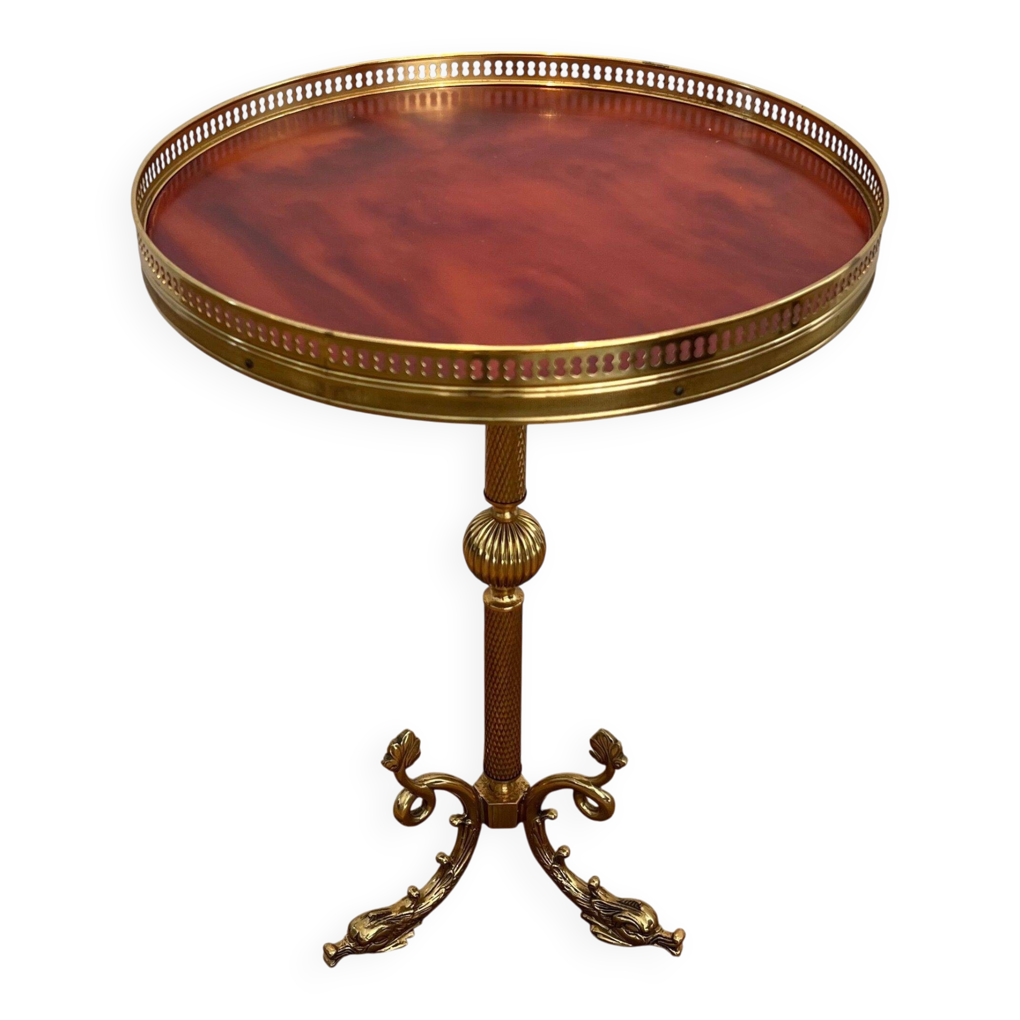 A round, neoclassical-style brass side table with a base decorated with dolphins and a red celluloid top encircled by an openwork gallery, attributed to the House of Jansen.