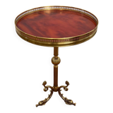 A round, neoclassical-style brass side table with a base decorated with dolphins and a red celluloid top encircled by an openwork gallery, attributed to the House of Jansen.